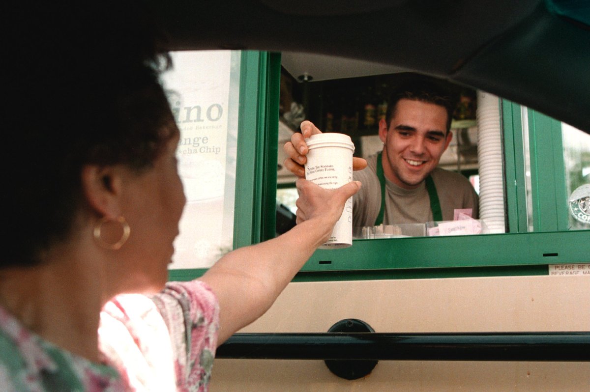 A Starbucks coffee employee hands a customer coffee through a drive-thru.
