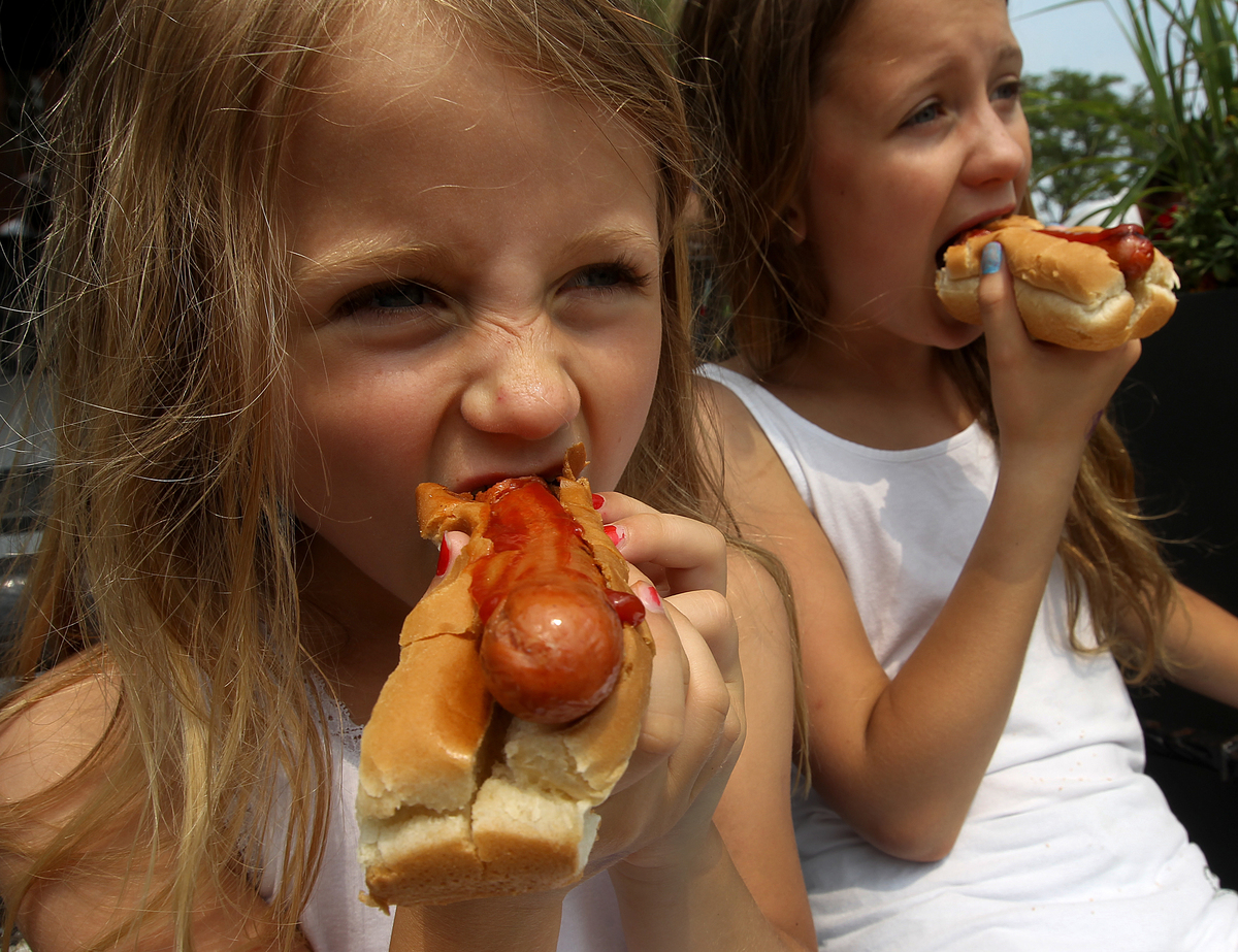 Two girls eat hot dogs.