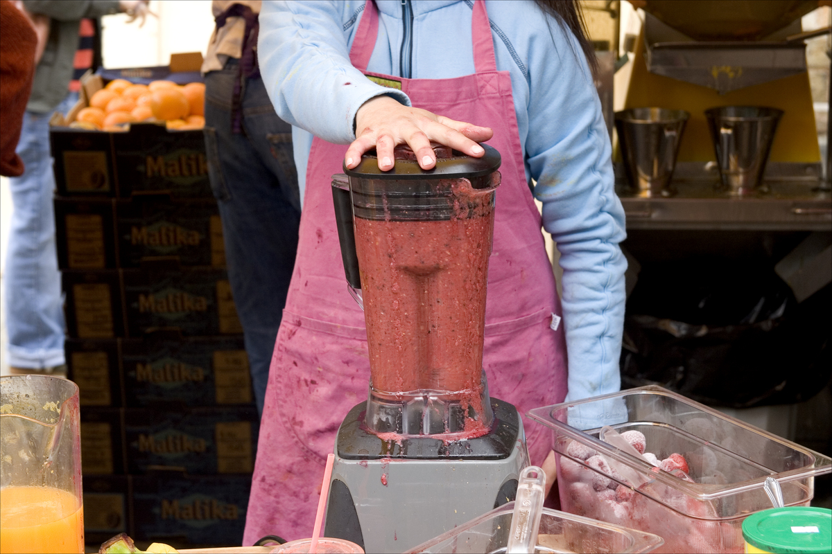 An employee blends a smoothie that's overflowing at a market.