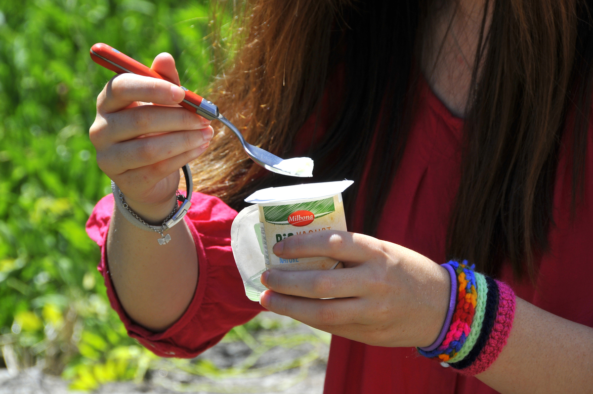 A teenager eats flavored yogurt.