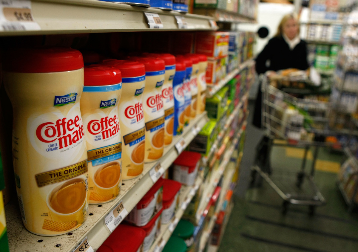 In the grocery store, powdered coffee creamers sit on a shelf.